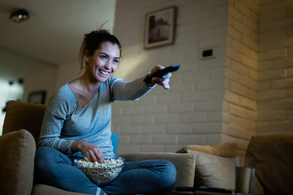 gas-pipeline happy woman using remote control while watching tv and eating po